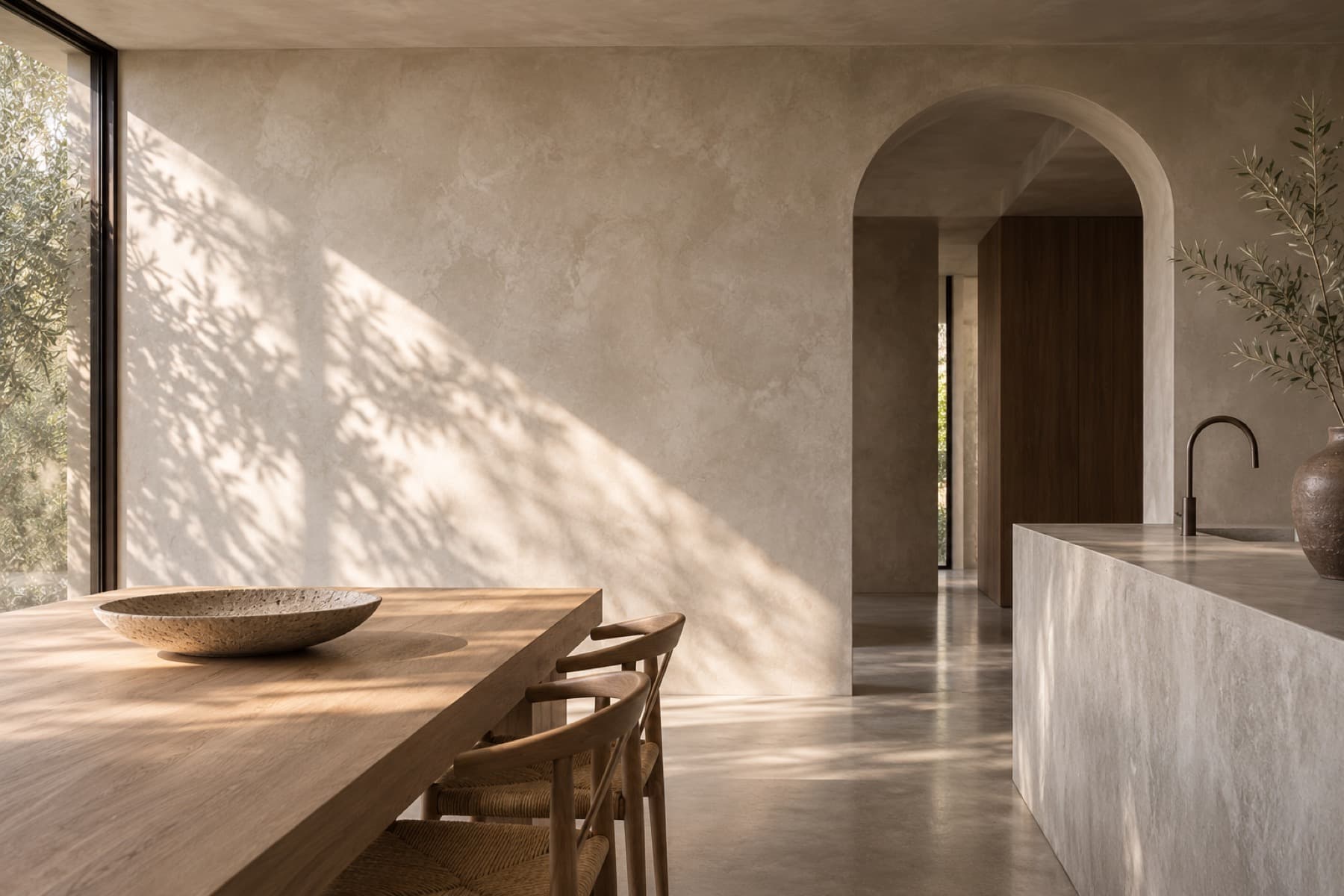 A sunlit interior with hand-finished limewash walls, a timber table and an arched doorway