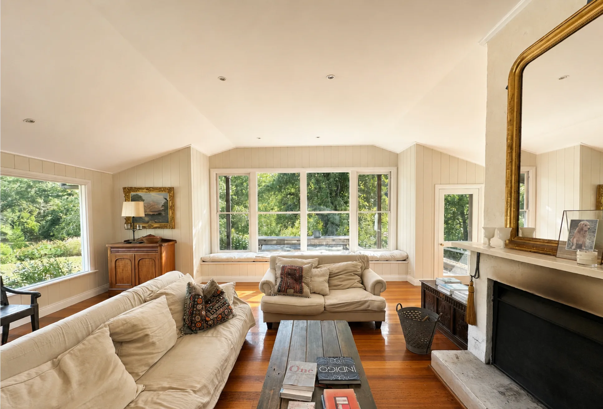 A board-lined living room in a period home, painted out in a soft off-white, with garden visible through the windows.