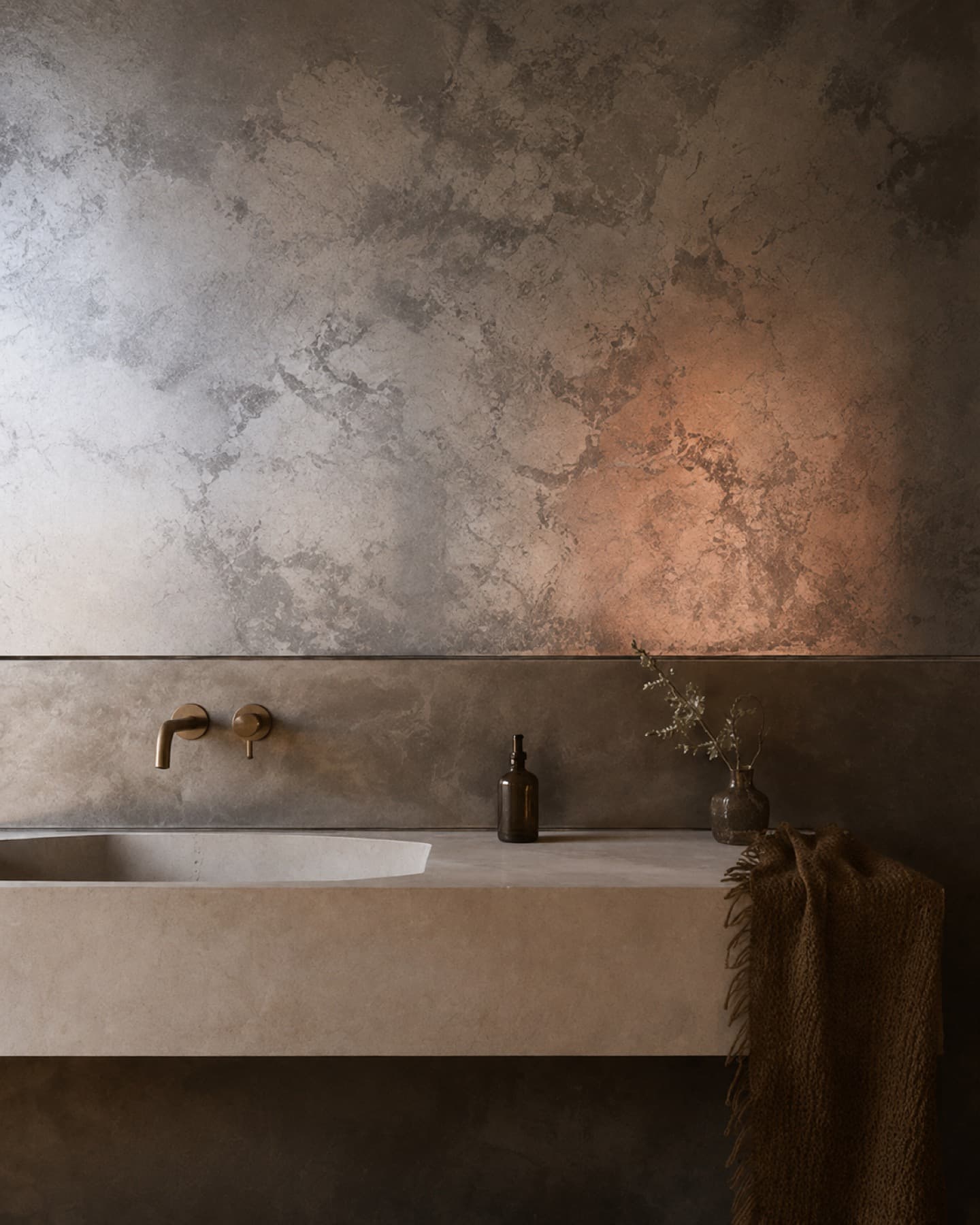 A reactive metallic patina finish on a bathroom wall, warm-lit above a stone vanity