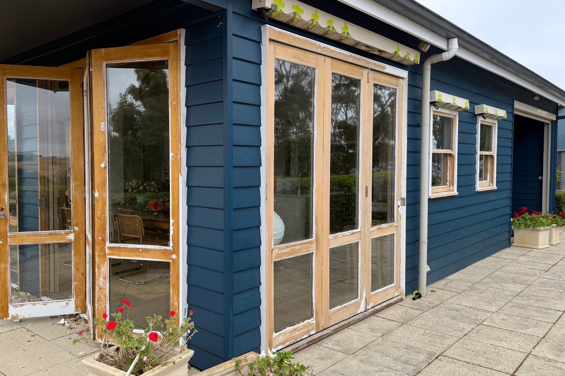 Timber doors and windows stripped back to bare timber, with failed paint remaining at the edges, set in a freshly painted weatherboard wall.