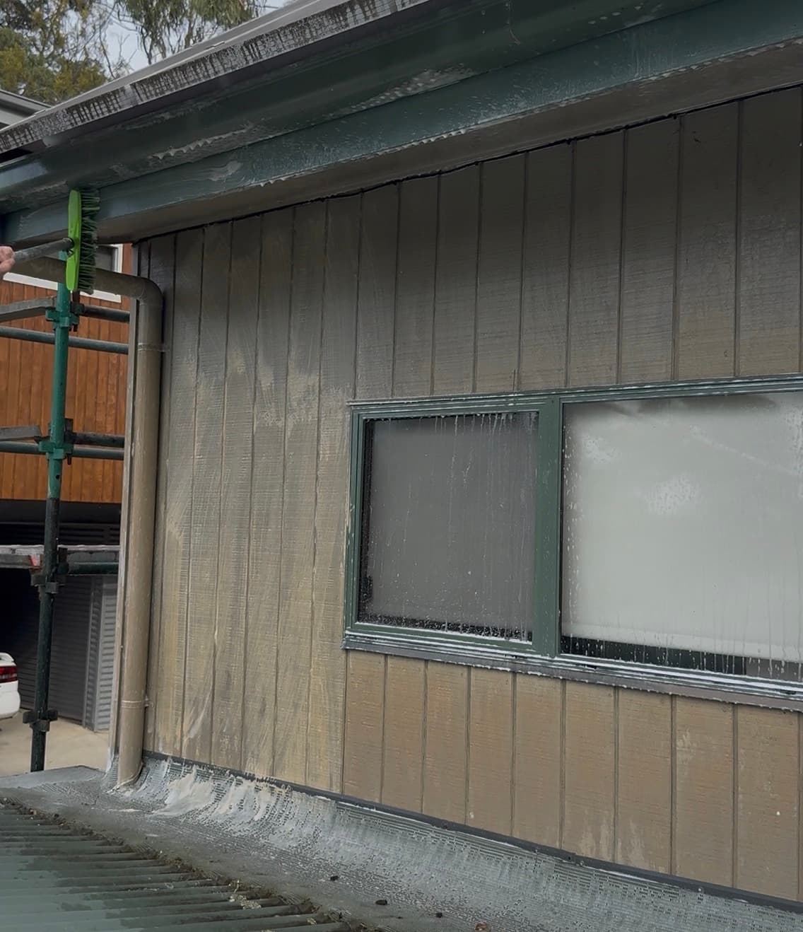 Chalked paint being washed from board cladding with a brush on a pole, run-off streaking the surface below.